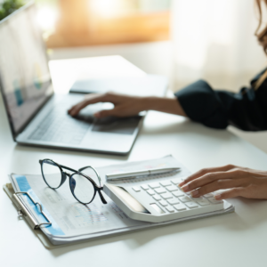 Personne qui travaille à l'ordinateur et fait des calculs à l'aide d'une calculatrice.